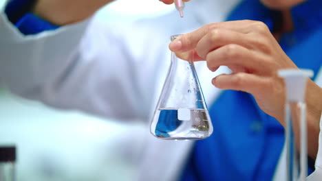 Mujer-Química-Agregando-Reactivo-Químico-En-Líquido-Puro-En-Un-Matraz-De-Vidrio